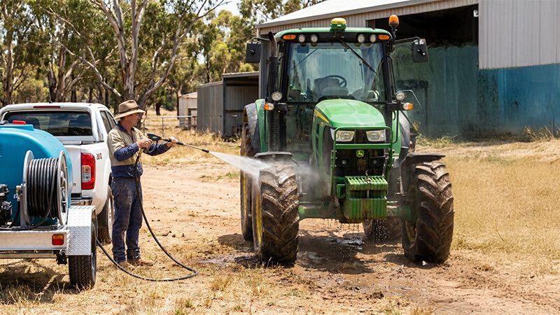 Man washing down a tractor on a farm using a Rapid Spray water cartage trailer