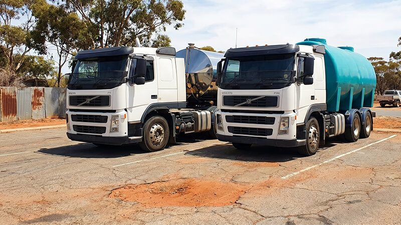 Two white water delivery trucks parked side by side, fitted with stainless steel and poly tanks for potable water transport and delivery